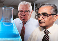 Monroe Wall (left) and Mansukh Wani (right) observe a beaker of Camptothecin dissolved in chloroform and methanol as it flouresces in UV light.